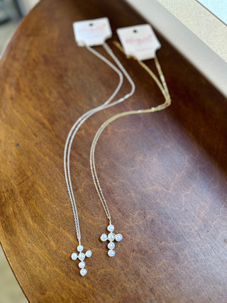 Two delicate pearl cross pendant necklaces displayed on a wooden surface with brand tags.