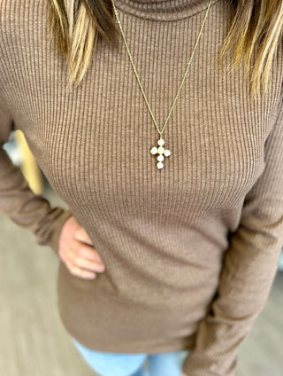 Gold cross pendant necklace with circular stone details worn over a ribbed turtleneck sweater.