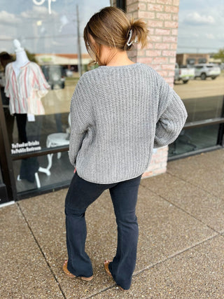 Woman wearing a chunky knit cardigan sweater with dark flare jeans, back view.
