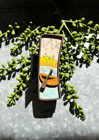 Handmade hair clip featuring painted boat scene with lake and sunset design on succulent background