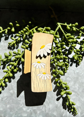 Handmade wooden hair clip with white daisy flower design on natural wood grain background