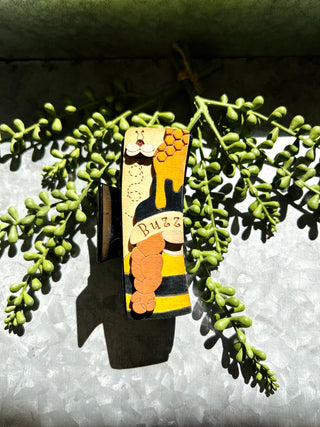 Handmade wooden hair clip with bee and honeycomb design displayed on succulent plant background