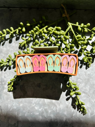 Handmade hair clip featuring colorful flip-flop design displayed on succulent plant in natural sunlight