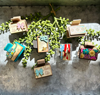 Handmade hair clips with various decorative designs including flowers, patterns, and text displayed on succulent plant