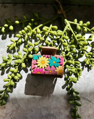 Handmade hair clip with colorful floral pattern displayed among green succulent plant vines.