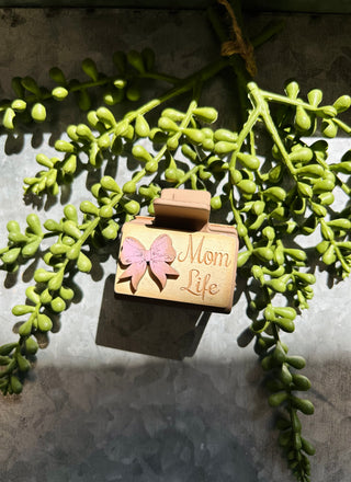 Handmade wooden hair clip with pink bow design and "Mom Life" text on succulent background