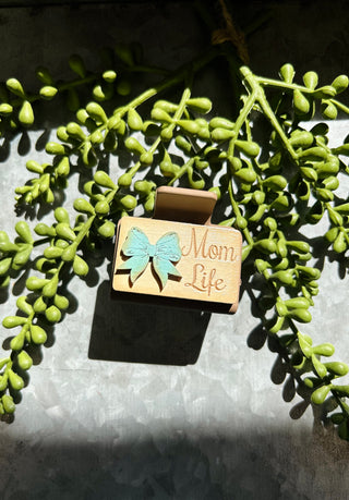 Handmade wooden hair clip with butterfly design and "Mom Life" text surrounded by green succulent plants