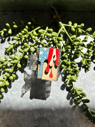 Handmade hair clip with American flag design featuring stars and stripes pattern displayed with green succulent plants