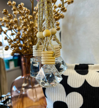 Crystal hanging car diffuser with wooden beads and rope suspended near decorative golden branches
