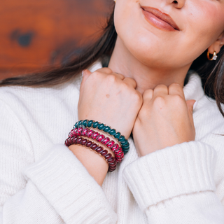 Woman wearing a stack of TELETIES large spiral hair ties on her wrist, paired with a cozy white sweater.