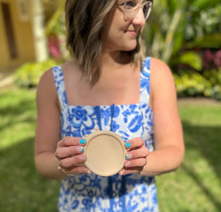 Woman wearing blue floral maxi dress holding round compact mirror outdoors in garden setting