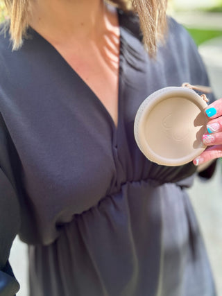 Woman in dark wrap dress holding coffee cup, showing elegant casual styling and colorful manicure.