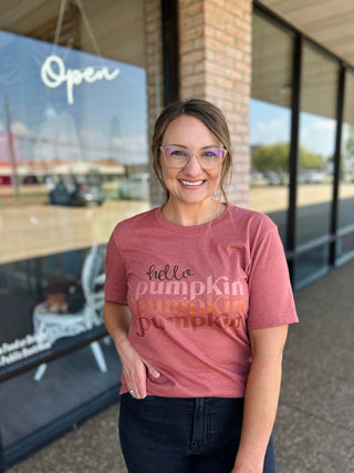 Woman smiling outside boutique wearing a "Hello Pumpkin" graphic tee with dark jeans.