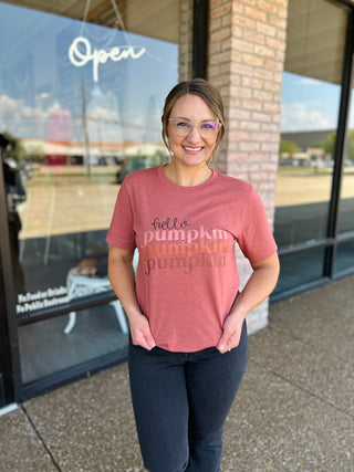 Woman smiling outside boutique wearing a "Hello Pumpkin" graphic tee with dark jeans.