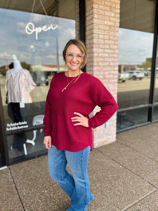 Woman wearing a long-sleeve waffle-knit sweater with curved high-low hem, paired with jeans.