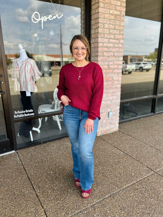 Woman wearing a relaxed waffle-knit sweater with high-low hem, paired with jeans.