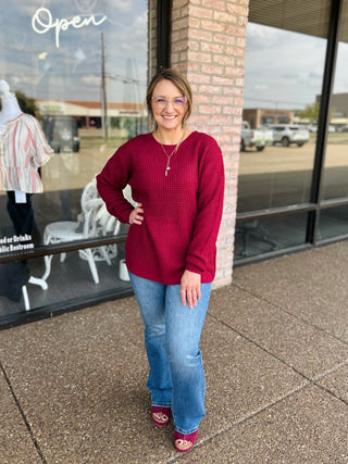 Woman wearing a relaxed waffle-knit sweater with high-low hem, paired with flared jeans.