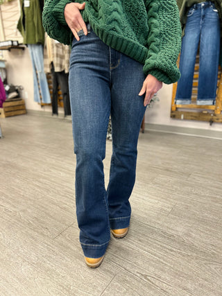 Person wearing dark blue high-rise flare jeans with green cable knit sweater in retail store setting.