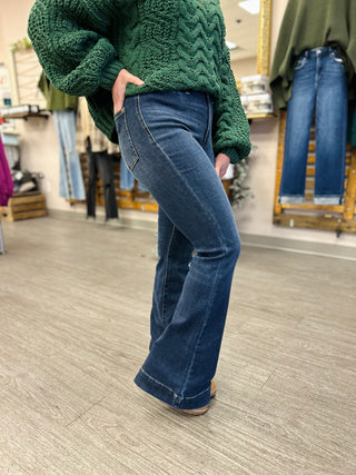 Person wearing Judy Blue high rise dark wash flare jeans with green cable knit sweater in clothing store.