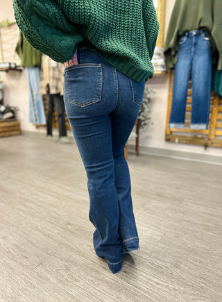 Woman wearing dark blue high-rise flare jeans with green knit sweater in casual retail setting.