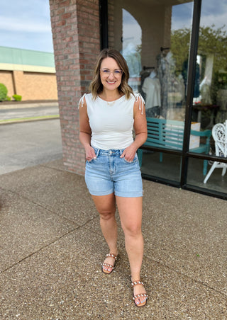Woman wearing high-rise cuffed denim shorts with white top, standing outside storefront