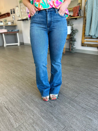 Woman wearing high-rise dark wash slim flare jeans with colorful top and platform sandals in modern room.