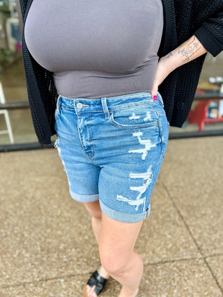 Woman wearing distressed denim shorts with rips and cuffed hems, paired with gray top and cardigan.