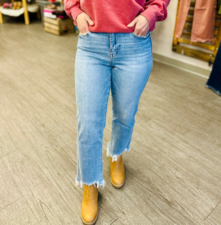 Person wearing high-rise cropped straight jeans with frayed hem detail and pink sweatshirt in retail store.
