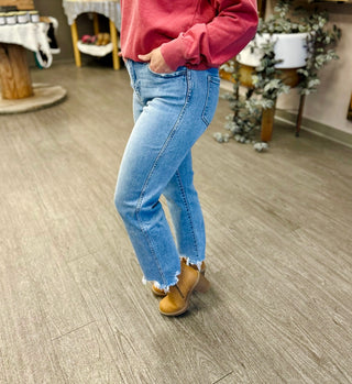 Person wearing high rise cropped straight jeans with frayed hem detail and brown boots in casual indoor setting.