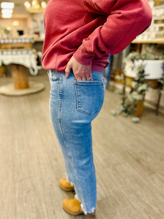 Person wearing high-rise straight leg jeans with frayed hem detail and red sweatshirt in casual setting.