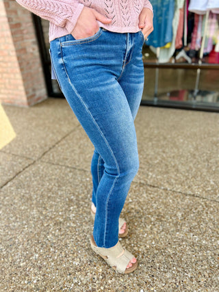 Woman wearing high-rise medium wash slim straight jeans with pink knit sweater and beige sandals.