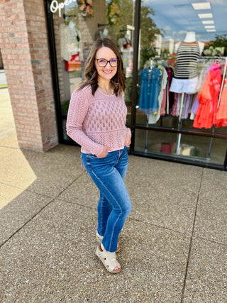 Woman wearing high rise medium wash slim straight jeans with pink sweater standing outside clothing store.