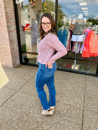 Woman wearing high rise medium wash slim straight jeans with pink sweater standing outside boutique storefront.
