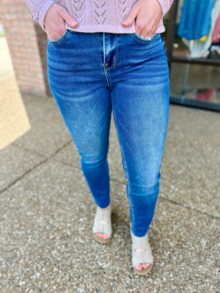 Woman wearing medium wash high rise slim straight jeans with purple sweater and white sandals.