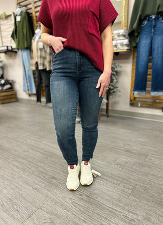 Woman modeling high-rise skinny jeans with step hem and red knit top in clothing store