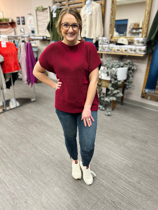 Woman wearing burgundy sweater and dark skinny jeans with white sneakers in boutique setting