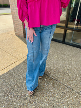 Woman wearing high rise wide hem pintuck flare jeans with bright pink top and platform sandals.