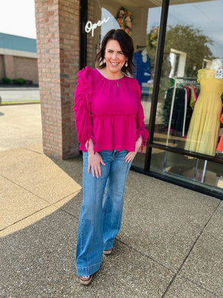 Woman wearing bright pink ruffled blouse and wide-leg flare jeans standing outside boutique storefront