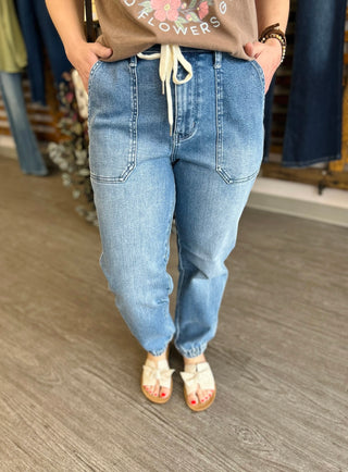 Woman wearing high-waisted denim joggers with drawstring waist and elastic cuffs in casual store setting.