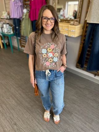 Woman wearing high-waisted denim joggers with drawstring waist and brown floral graphic tee in clothing store