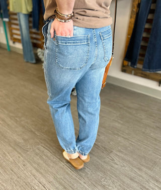 Person wearing light blue high-waisted denim joggers with elastic cuffs and tan shoes in store setting.