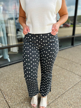 Woman wearing high-rise polka dot crop flare jeans paired with a cream knit top and metallic sandals.