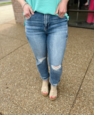 Woman wearing distressed high-rise cropped straight leg jeans with rips at knees and frayed hem.