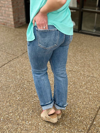 Woman wearing light blue cropped straight jeans with rolled cuffs and mint green top, hand in back pocket.