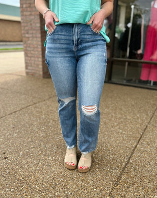 Woman wearing distressed high-rise cropped straight leg jeans with ripped knees and frayed hems.