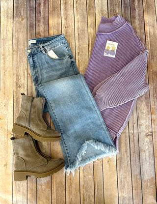 Distressed denim jeans with frayed hem styled with purple sweater and tan boots on wooden background