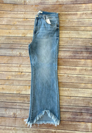 Risen highrise cropped bootcut jeans with frayed hem laid flat on rustic wooden background