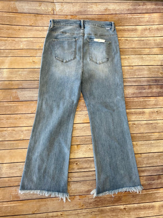 Risen high-rise cropped bootcut jeans with frayed hem displayed flat on wooden background