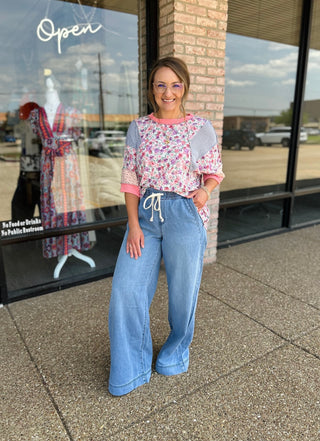 Woman wearing high-rise pull-on extra wide leg jeans with drawstring waist, styled with floral top.