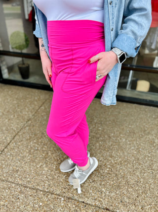 Woman wearing bright pink fitted joggers with white sneakers and denim jacket, showing casual comfortable style.